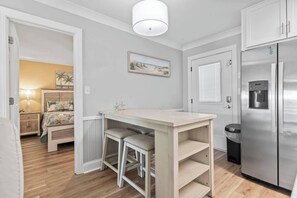 Una cocina compacta con refrigerador integrado, una pequeña mesa de comedor y un banco.