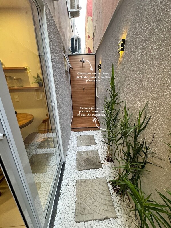 A narrow outdoor corridor with a wooden door, white pebbles, and green plants. - Flat Pé na Areia Iriri (Anchieta)