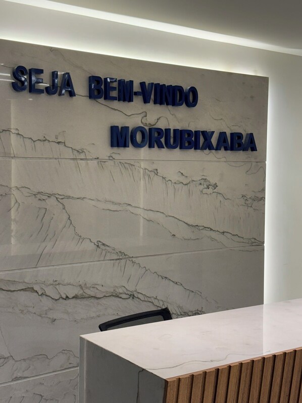A reception desk with a marble wall and a sign that reads "SEJA BEM-VINDO MORUBIXABA". - Flat Pé na Areia Iriri (Anchieta)