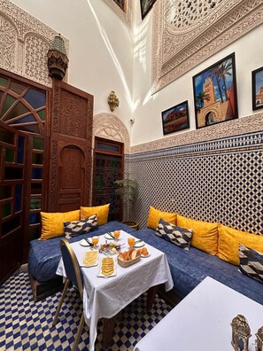 A room with intricate wall and ceiling designs, a checkered floor, and a table set with food and drinks. - Riad Dar Rabha (Fes)