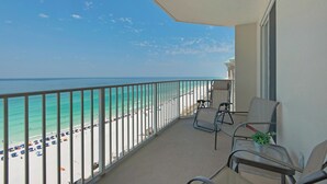 Een balkon met uitzicht op het strand en de oceaan. Er staan stoelen en een klein tafeltje met een plant.