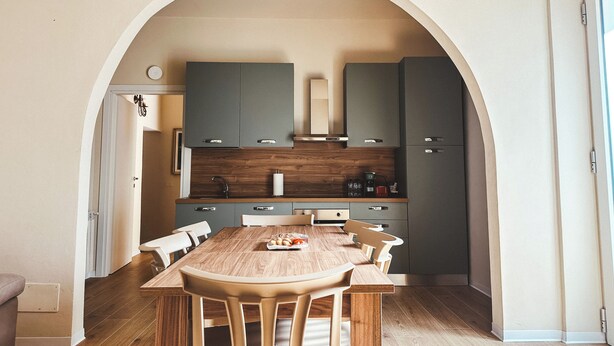 A modern kitchen with an arched doorway, wooden table, and matching chairs. - Casa da Victoria - Apartment 1 (Castrezzato)