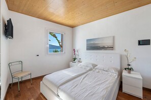Une chambre à coucher avec un lit, une fenêtre donnant sur un beau paysage, une chaise, une table de chevet et une commode.