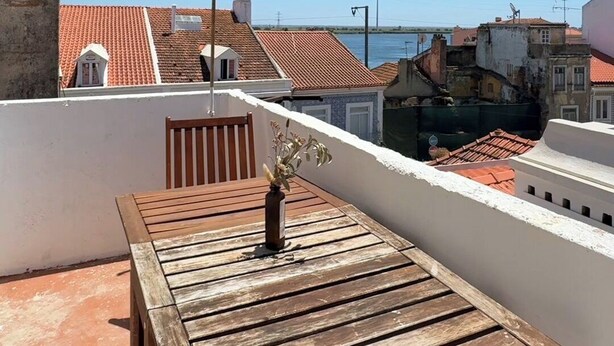 A wooden table with a vase on a rooftop terrace with a clear view of the sea and buildings in the background. - Charming Apartment with River Views & Sunny Terraces near Lisbon (Vila Franca de Xira)