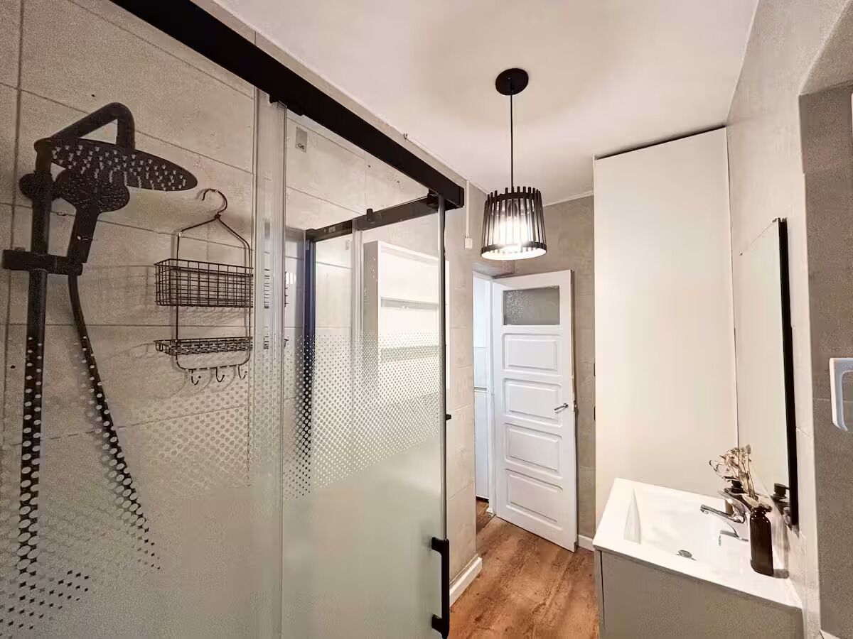 Une salle de bain moderne avec une douche à parois de verre, un luminaire suspendu et un lavabo blanc avec un miroir.