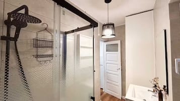 Une salle de bain moderne avec une douche à parois de verre, un luminaire suspendu et un lavabo blanc avec un miroir.