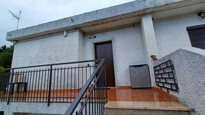 Un edificio con fachada blanca, una puerta marrón y un pequeño balcón con barandilla de metal.