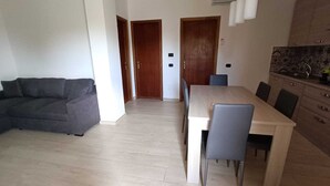 Una sala de estar moderna con un sofá gris, una mesa de comedor de madera con sillas y una cocina con armarios y una encimera.