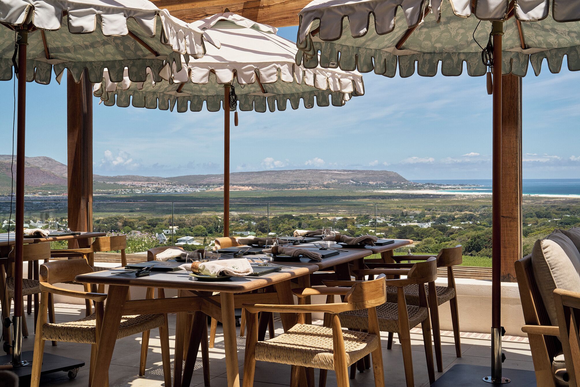 Un espace de restauration en plein air avec des tables et des chaises en bois, des parasols et une vue panoramique sur le paysage.