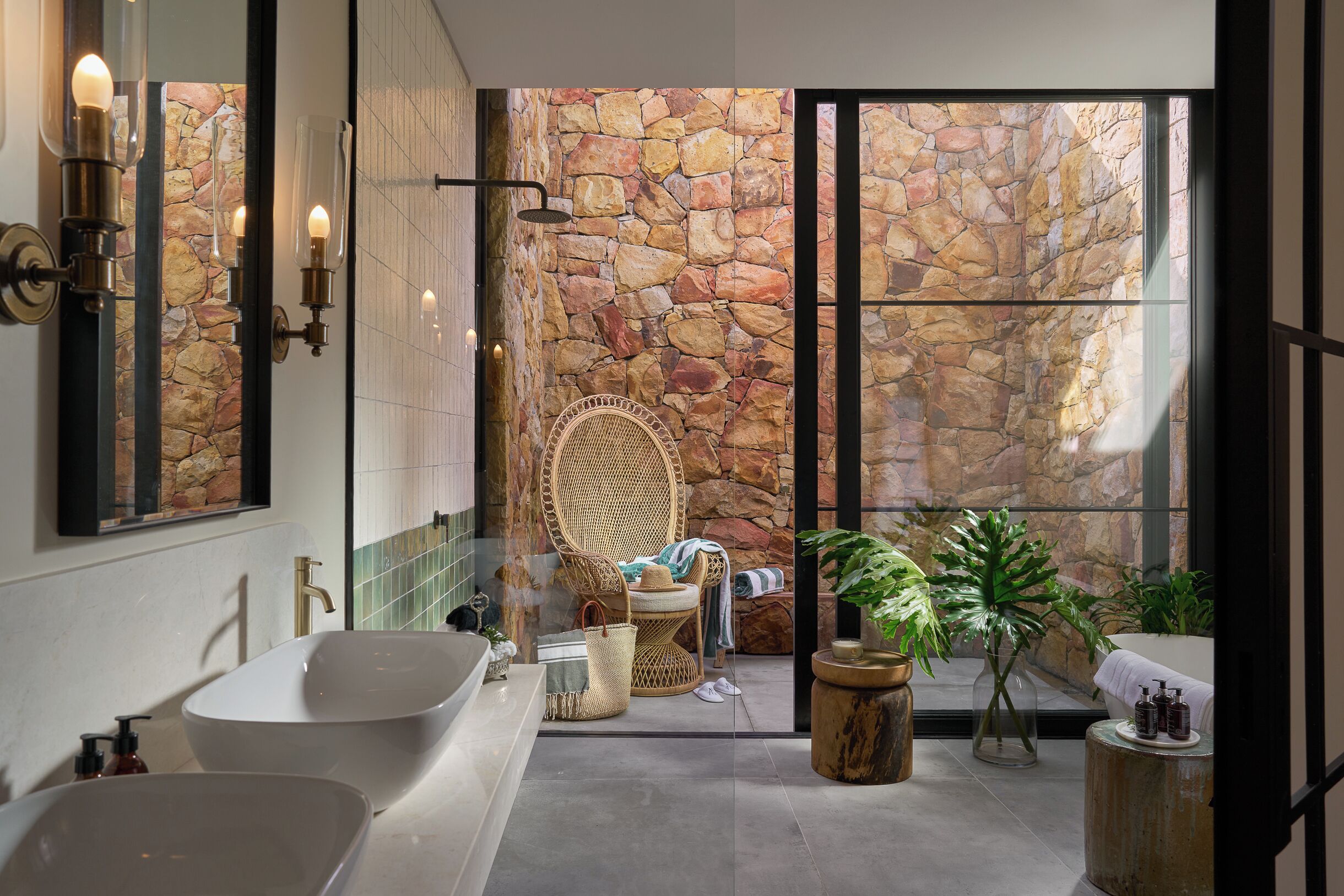Un baño moderno con una bañera grande, un lavamanos independiente, una silla de mimbre y una pared de piedra.