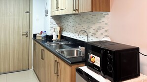 A kitchen with wooden cabinets, a black countertop, a stainless steel sink, a microwave, and a small shelf with decorative items. - Crizzy's Hub Crizel @ Shore Residences with Balcony + Amenity View (Pasay City)
