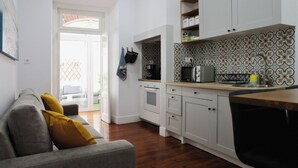 Une cuisine moderne avec des meubles blancs, un four à micro-ondes et un évier. Le salon est doté d’un canapé gris avec des coussins jaunes.