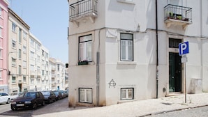 Une rue bordée de voitures garées, un immeuble avec un panneau indiquant un parking (« P »), et une enseigne « LULA DAS BRASIL » sur l’immeuble.