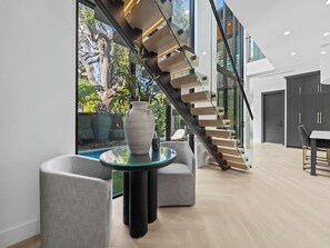 Un interior moderno con una escalera de cristal, una mesa redonda de cristal con un florero y sillones tapizados grises.