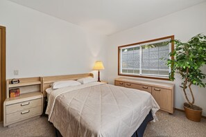 A bedroom with a bed, bedside table, lamp, dresser, and a potted plant.