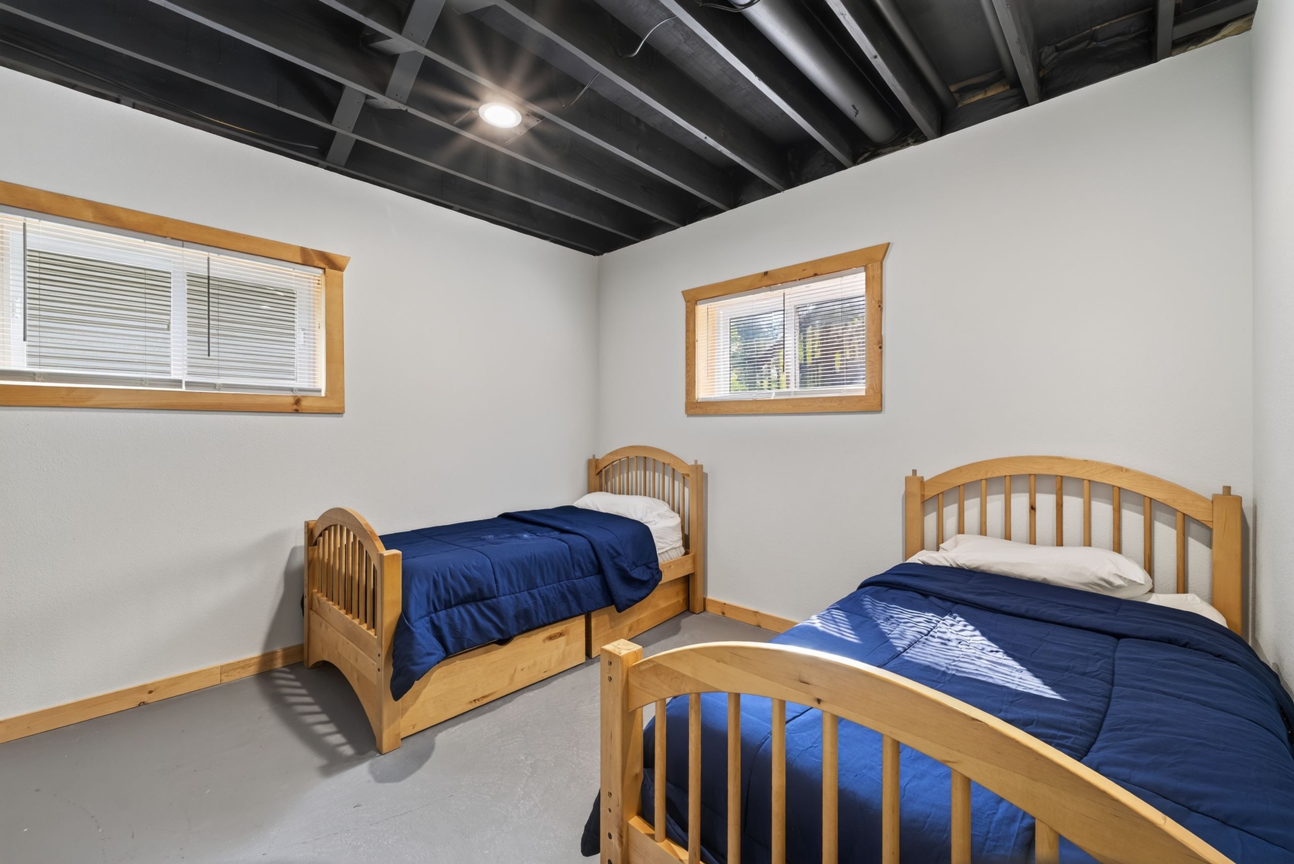 A room with two wooden beds, white walls, and a sloped ceiling with exposed beams.