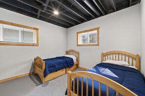 Une pièce avec deux lits en bois, des murs blancs et un plafond en pente avec des poutres apparentes.