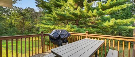 A wooden deck with a picnic table and grill, surrounded by trees.