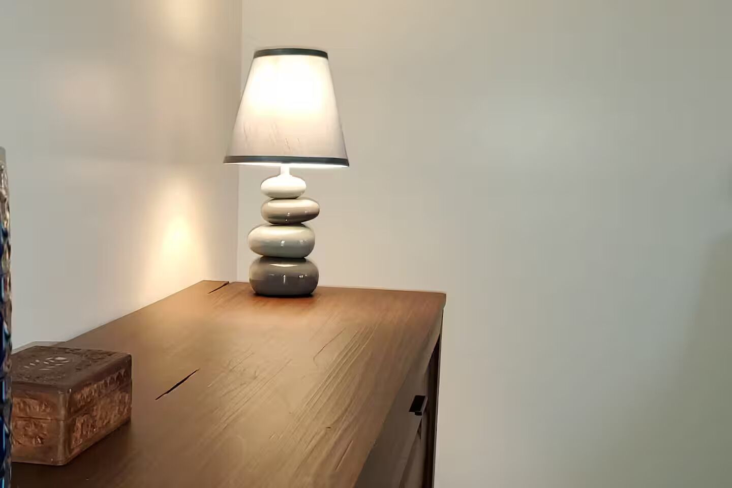 Una mesita de noche de madera con una lámpara y una caja decorativa.