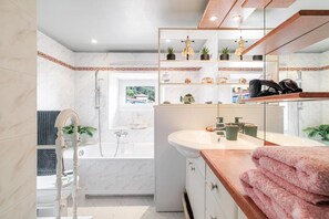 A modern bathroom with a bathtub, a vanity with a mirror, and shelves with plants and toiletries.
