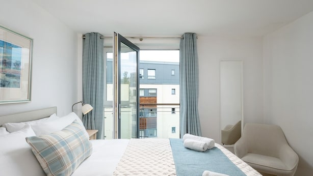 Une chambre d’hôtel moderne, dotée d’un grand lit, d’une chaise, d’un bureau et offrant une vue sur la ville grâce à une grande fenêtre.