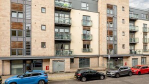 Un immeuble résidentiel à plusieurs étages, doté de balcons, d’un garage et d’un espace de stationnement avec des voitures.