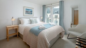Une chambre à coucher comprenant un lit, une table de chevet, une lampe, une fenêtre avec des rideaux et une chaise.