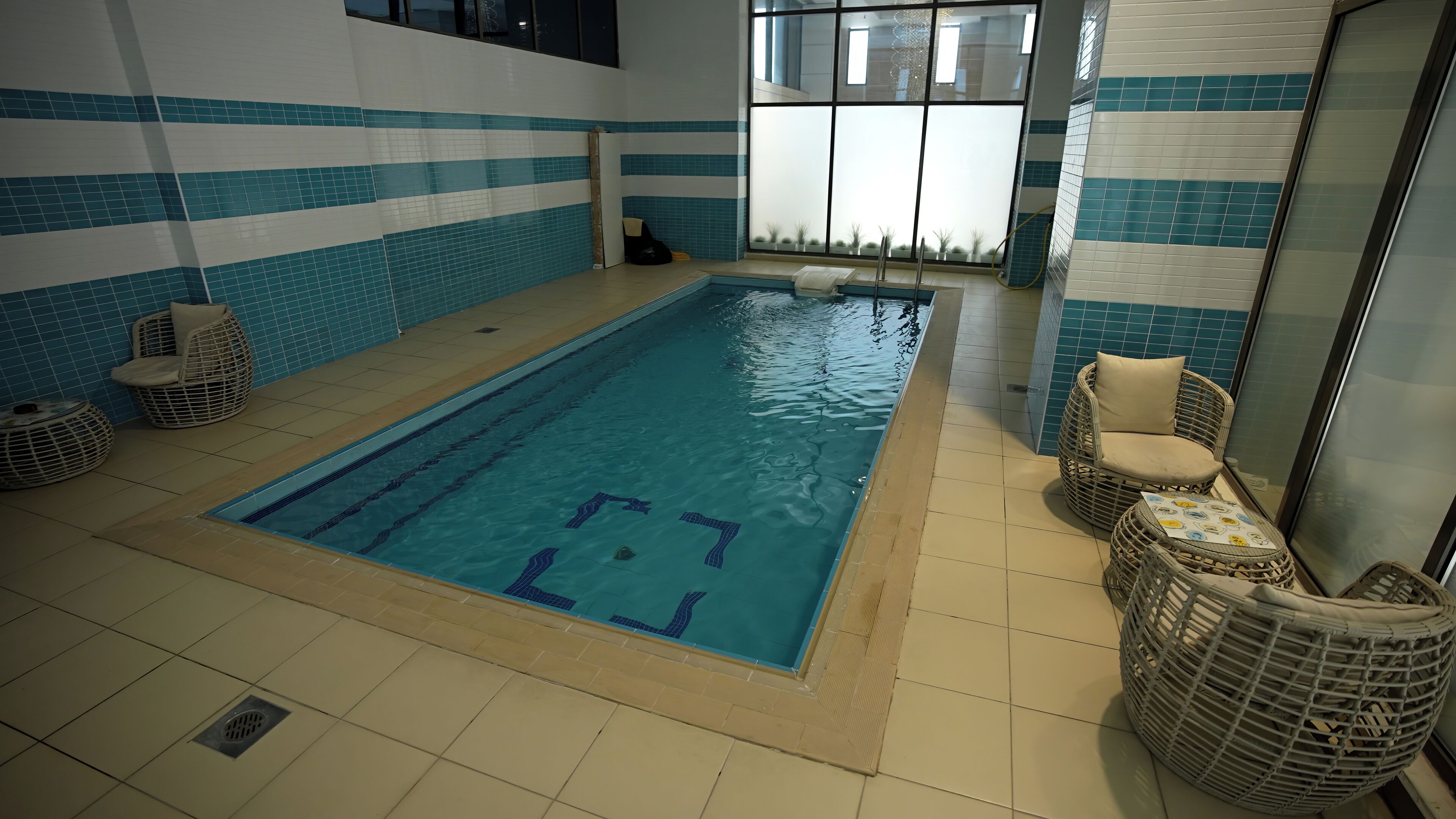 An indoor swimming pool with tiled walls and a clear view of the outside through large windows.