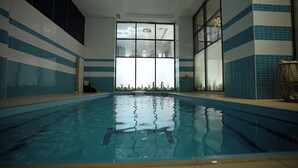 An indoor swimming pool with clear water, tiled walls, and large windows.