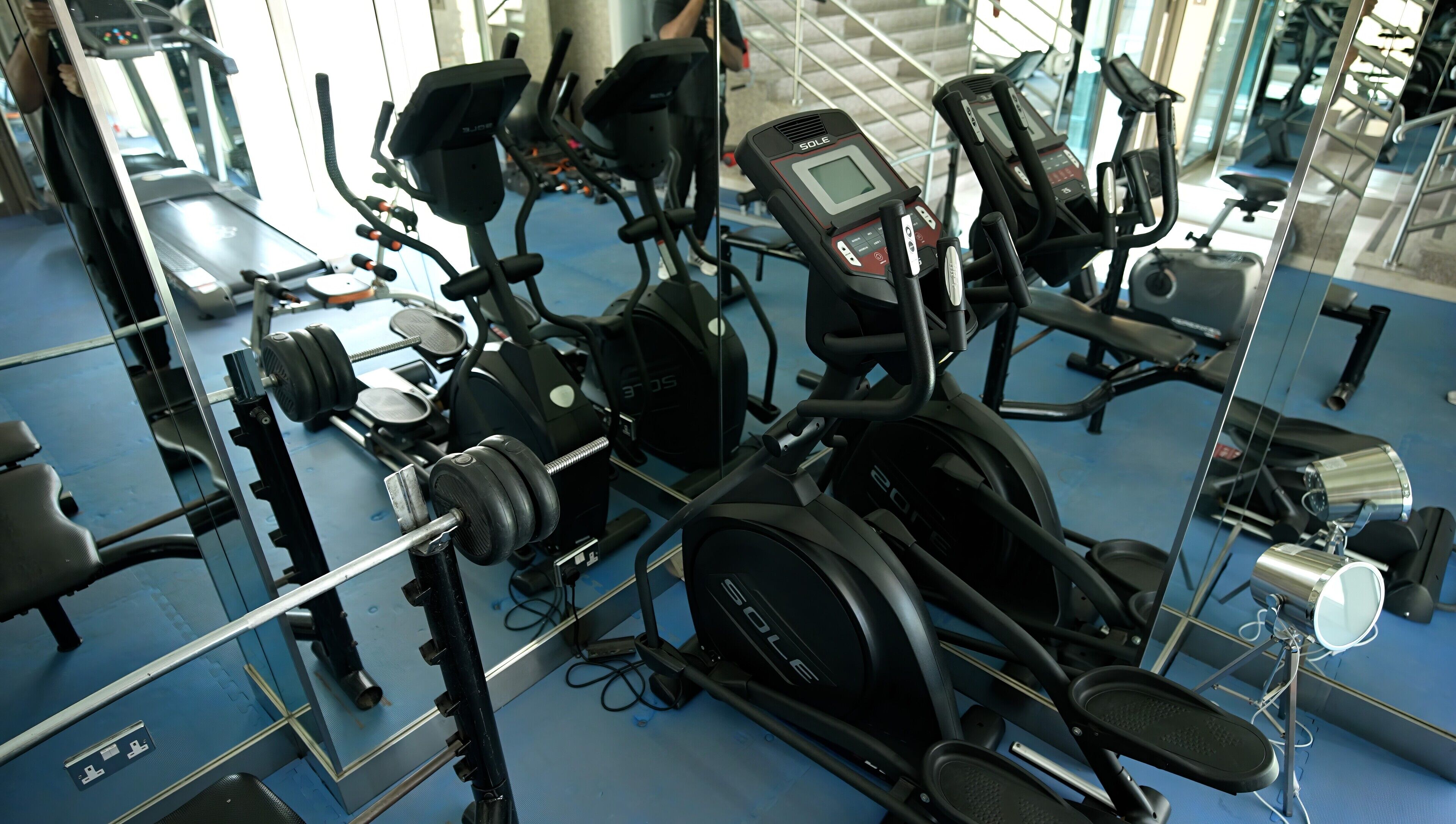 A gym with various exercise equipment including treadmills, elliptical machines, and weightlifting stations.