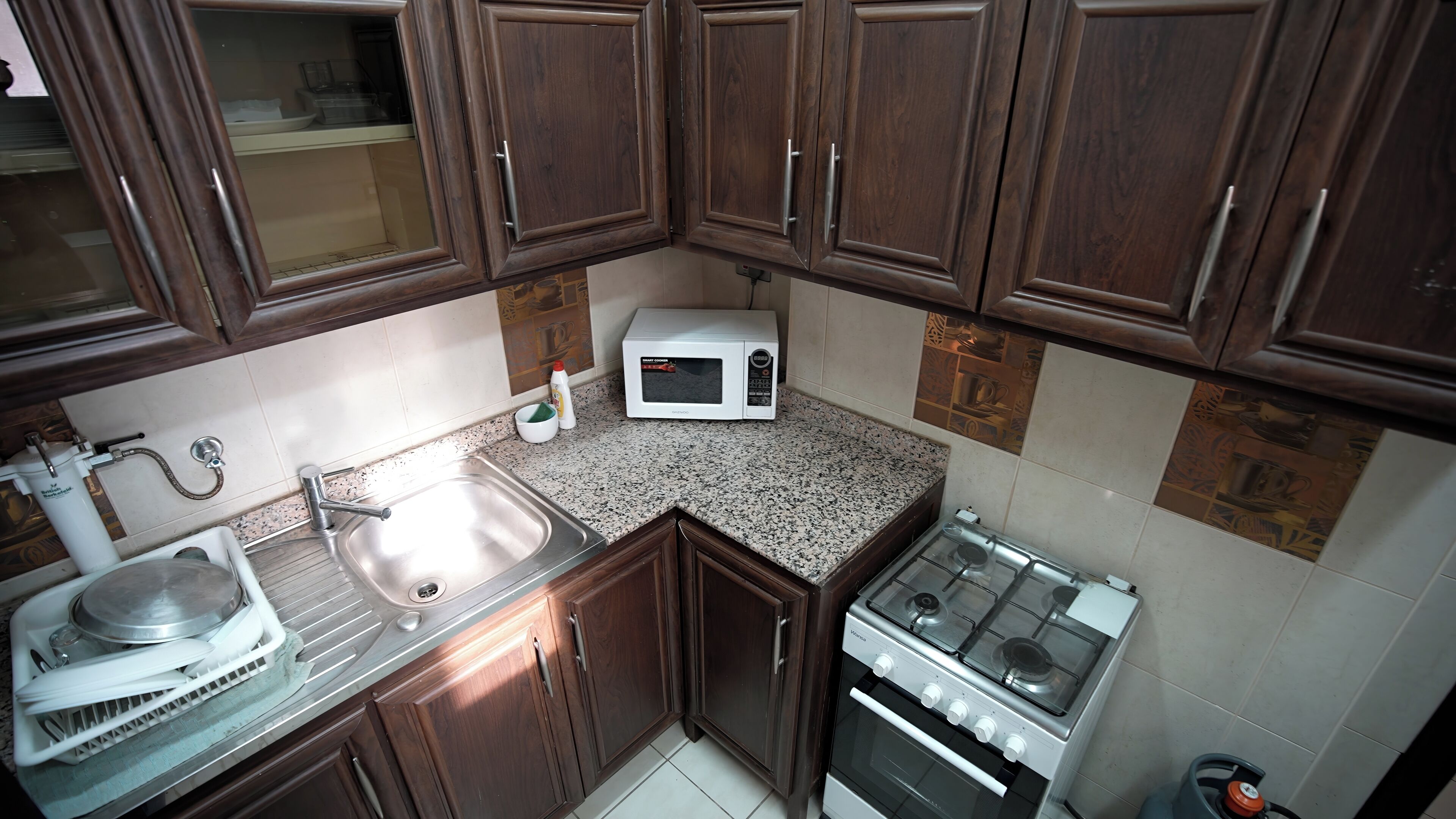 Una cocina con armarios de madera, un lavamanos de acero inoxidable, un microondas y una estufa a gas.
