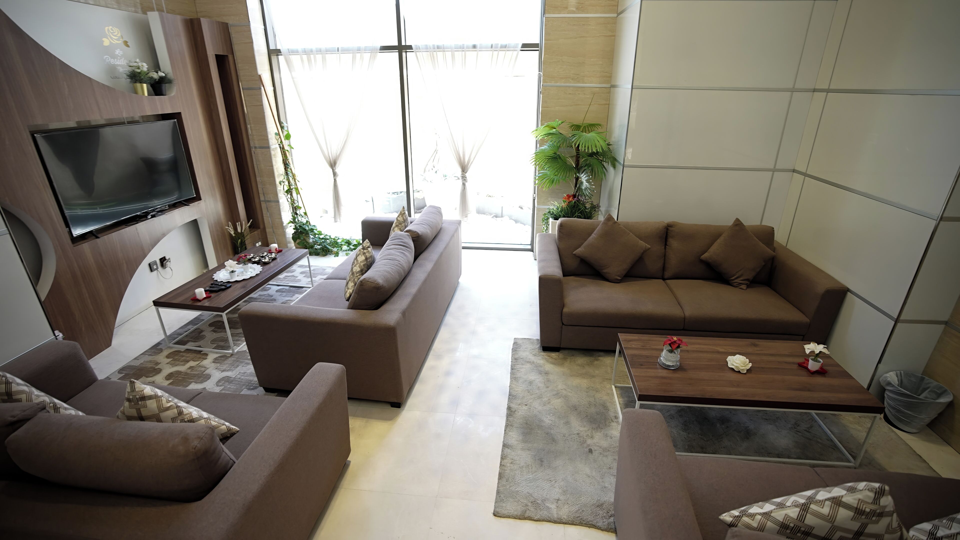 A modern living room with a flat-screen TV, two sofas, a coffee table, and a dining area with a table set for two.