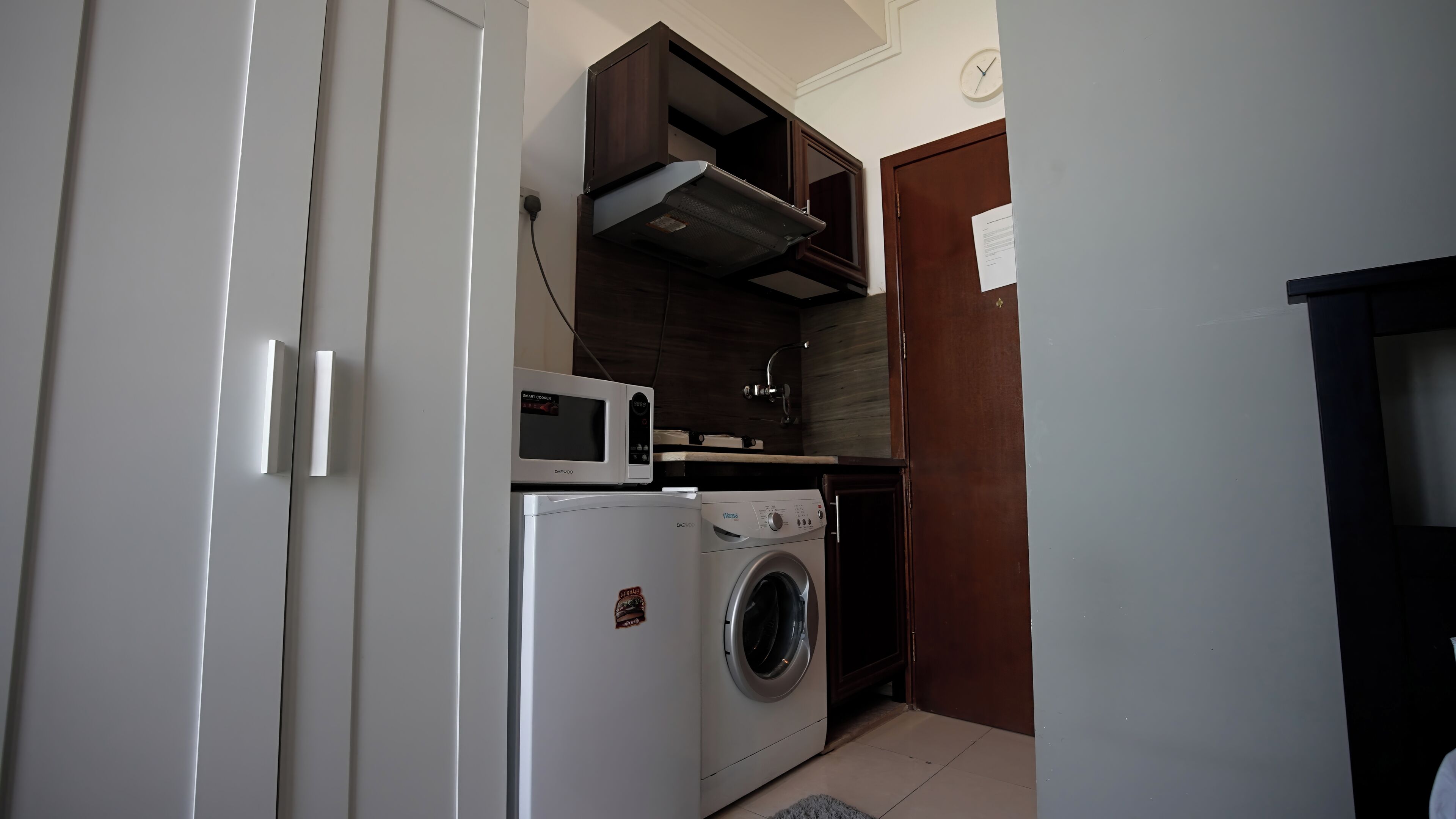 A compact kitchen with a microwave, a washing machine, and a small cabinet.