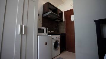 A compact kitchen with a microwave, a washing machine, and a small cabinet.