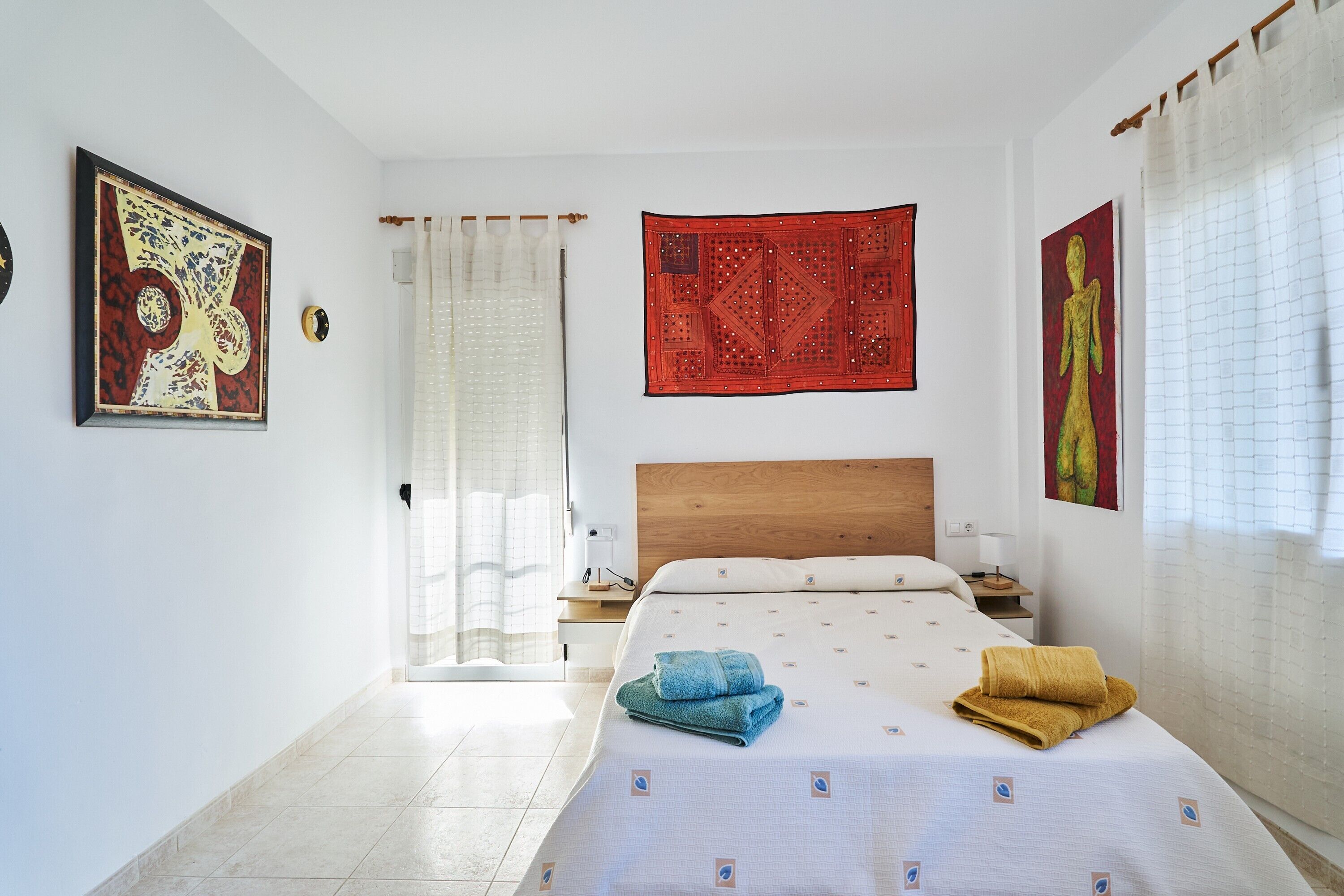 Una habitación de hotel con una cama, una mesita de noche, un cabecero de madera, un tapiz rojo y un cuadro en la pared.