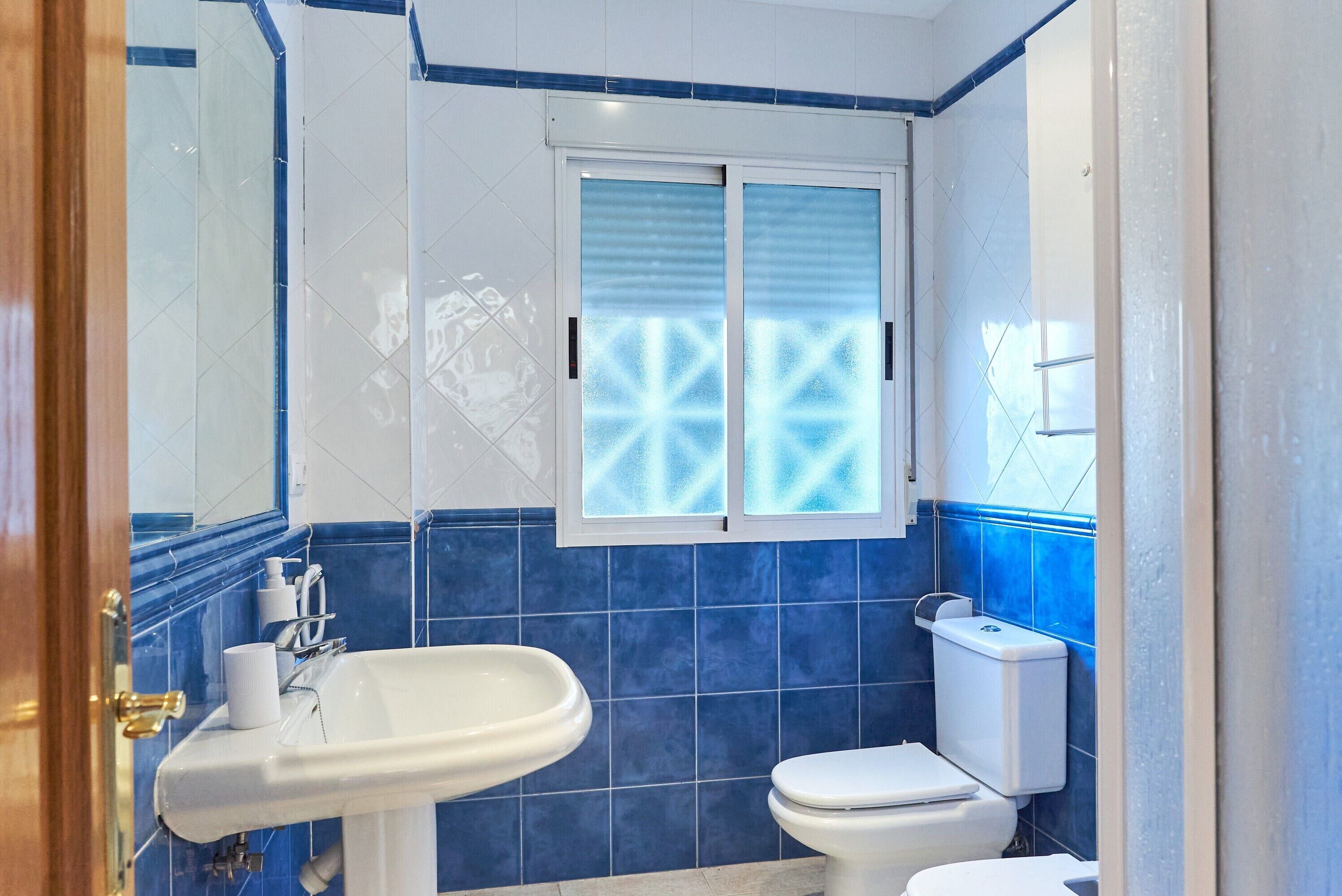 Une salle de bain avec un lavabo blanc, des toilettes et une fenêtre en verre dépoli.