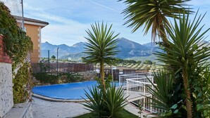 Un espace piscine offrant une vue sur les montagnes, entouré de verdure et délimité par une clôture blanche.