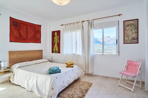 A bedroom with a bed, a chair, a window with a view, and artwork on the walls.