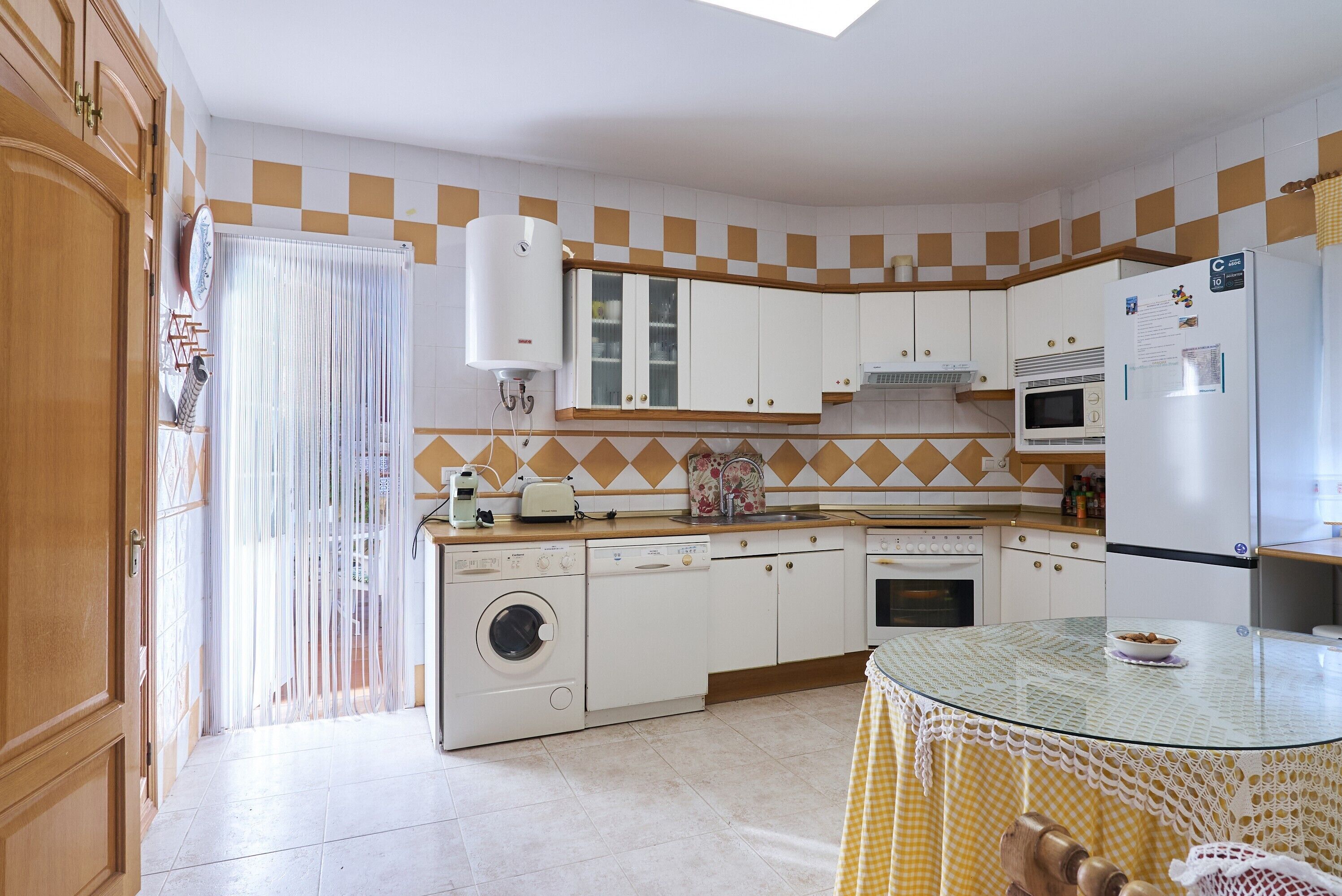 Une cuisine avec des meubles blancs, un lave-linge, un four à micro-ondes et un réfrigérateur.