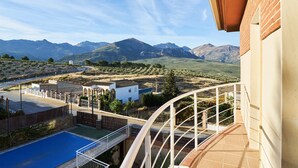 Un balcon avec vue sur les montagnes, une piscine et un bâtiment à la façade blanche.
