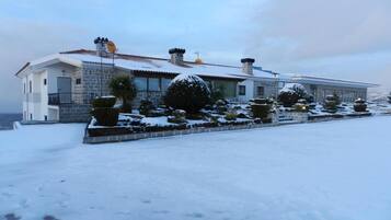 Una casa moderna con fachada de piedra, múltiples chimeneas y un paisaje cubierto de nieve.