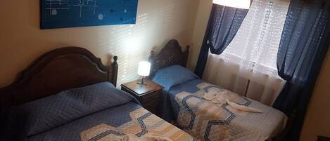 A hotel room with two beds, a nightstand, a wall art piece, and a window with curtains.
