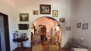 A living room with two armchairs, a coffee table, and a sofa. There is a kitchen visible through an archway. - Casa Bungavilia - Roots of Alentejo (Alvito)