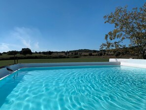A clear blue swimming pool with a view of a grassy landscape and trees in the background. - Casa Bungavilia - Roots of Alentejo (Alvito)