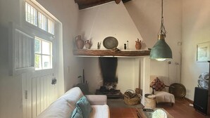A cozy living room with a wooden ceiling, a white sofa with blue cushions, a wooden coffee table, and a fireplace with a shelf above it. - Casa Bungavilia - Roots of Alentejo (Alvito)