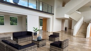 A spacious living area with wicker furniture, a potted plant, and a staircase. - Newly Luxury Condo in Cozumel! D'Maria Condos (Cozumel)