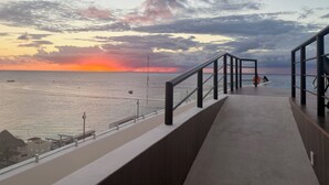 A balcony with a view of the sea at sunset, featuring a railing and a clear sky. - Newly Luxury Condo in Cozumel! D'Maria Condos (Cozumel)