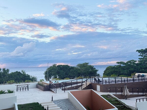 A rooftop pool area with a view of the sea, surrounded by greenery and modern outdoor furniture. - Newly Luxury Condo in Cozumel! D'Maria Condos (Cozumel)