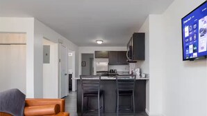 Una cocina moderna con armarios oscuros, un refrigerador de acero inoxidable y un televisor de pantalla plana montado en la pared.