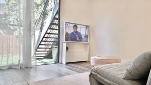 A modern living room with a sofa, a television, and a staircase leading to an outdoor area. - PP Garden (Bondi)